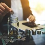 Closeup image of a businesswoman putting coins in a glass jar , calculating and stacking money for saving and financial concept